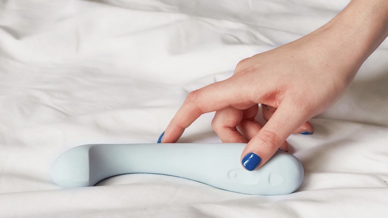 person picking up vibrator off bed 