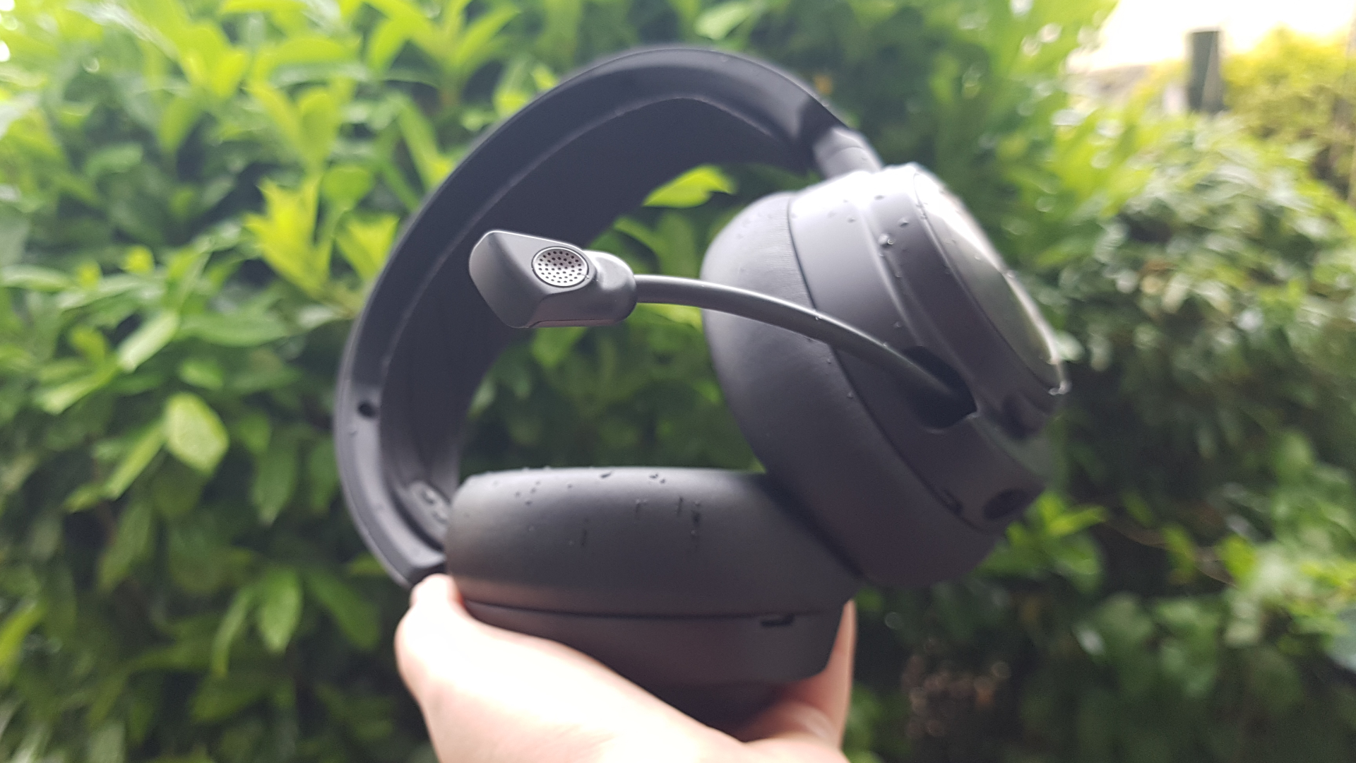 The SteelSeries Arctis Nova Pro wireless held up in front of a bush.