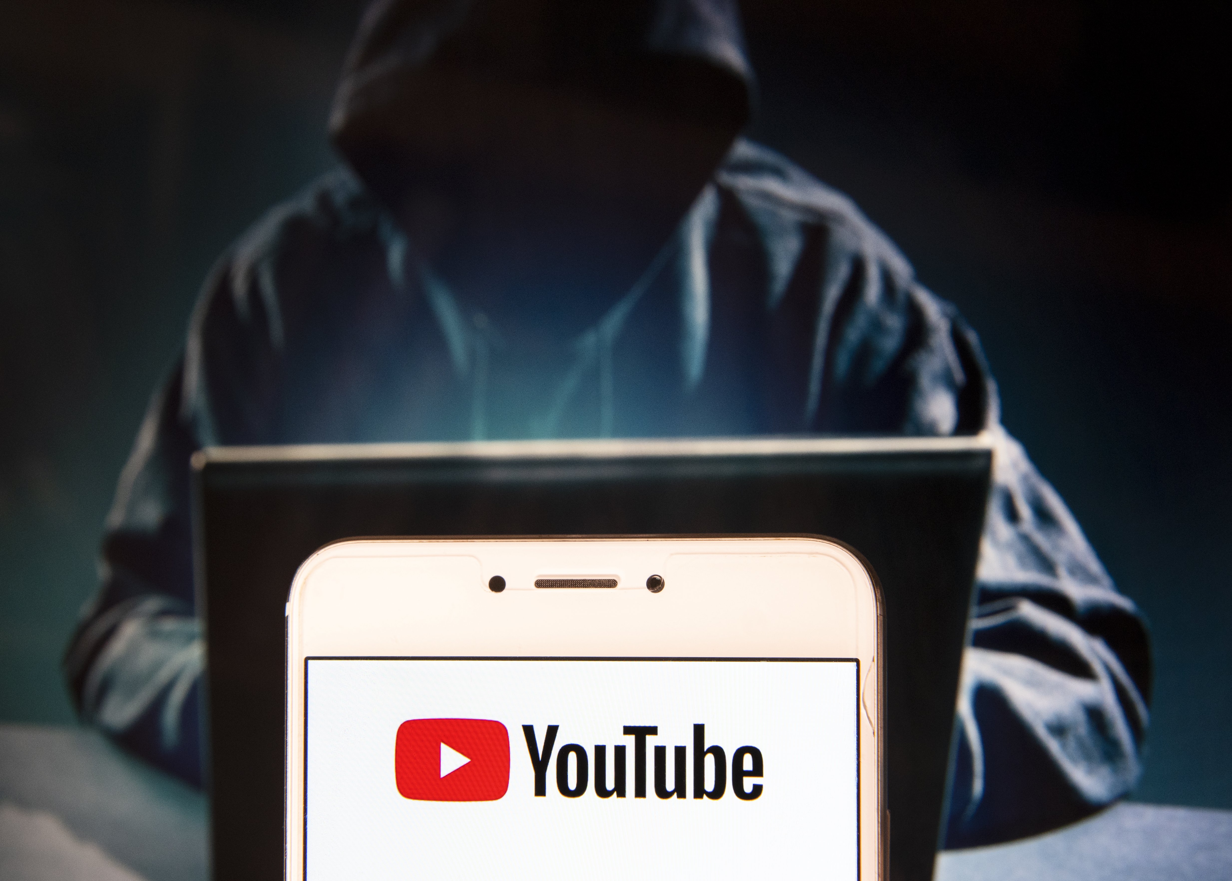 American video-sharing website Youtube logo is seen displayed on an Android mobile device with a figure of hacker in the background.