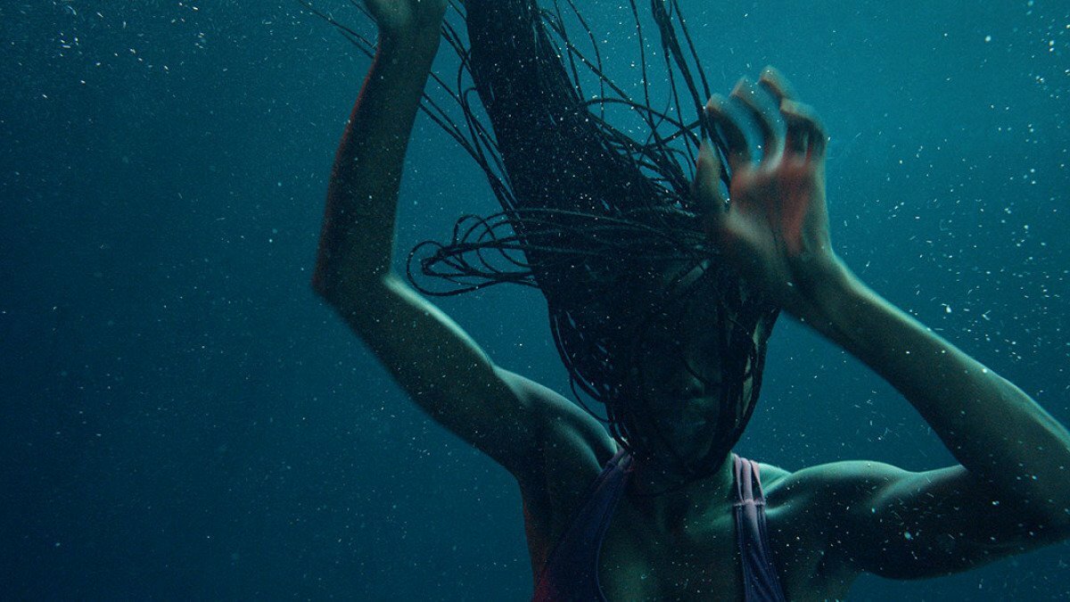 A woman with long braids floats underwater.