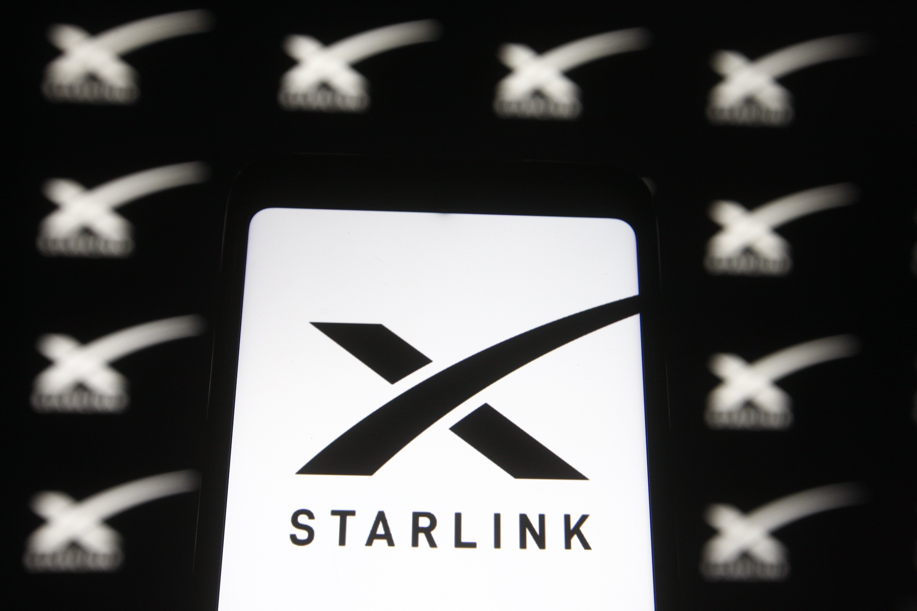 Starlink logo of a satellite internet constellation being constructed by SpaceX is seen on a smartphone and a pc screen