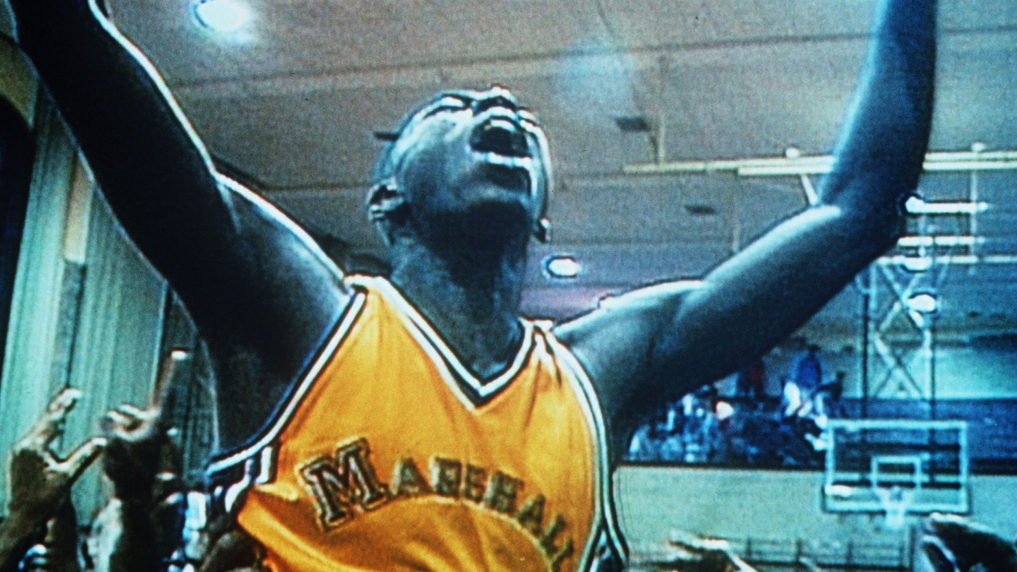 A man in a yellow basketball jersey raises his arms in victory.
