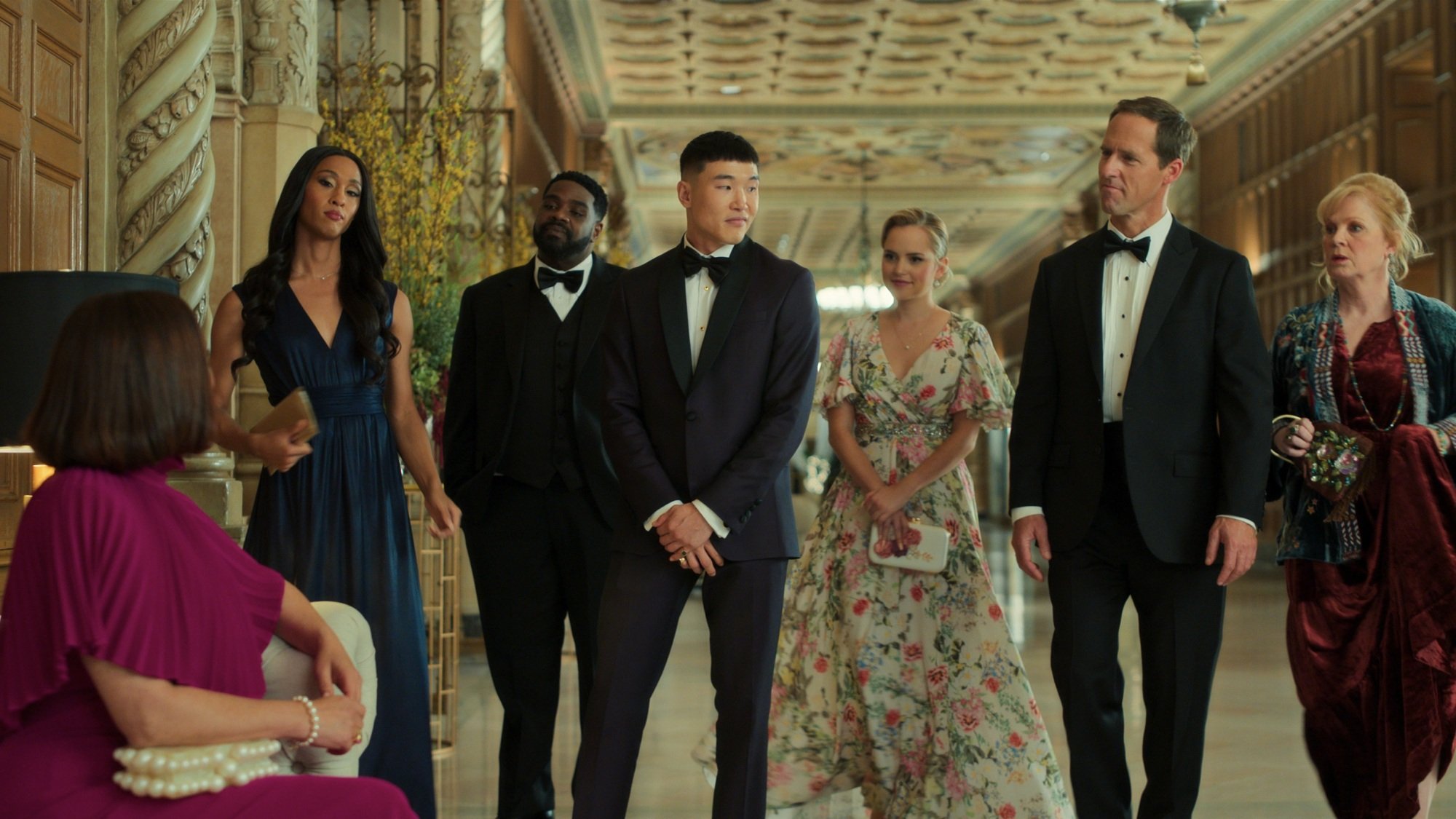 A group of people in fancy dresses and suits in a fancy hallway.