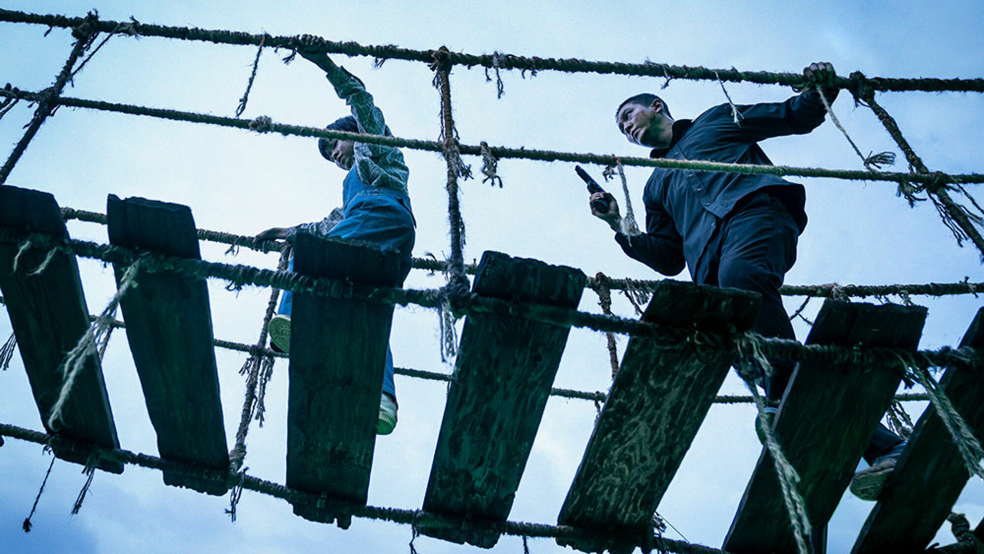 A man and a child walk across a rotting rope bridge.