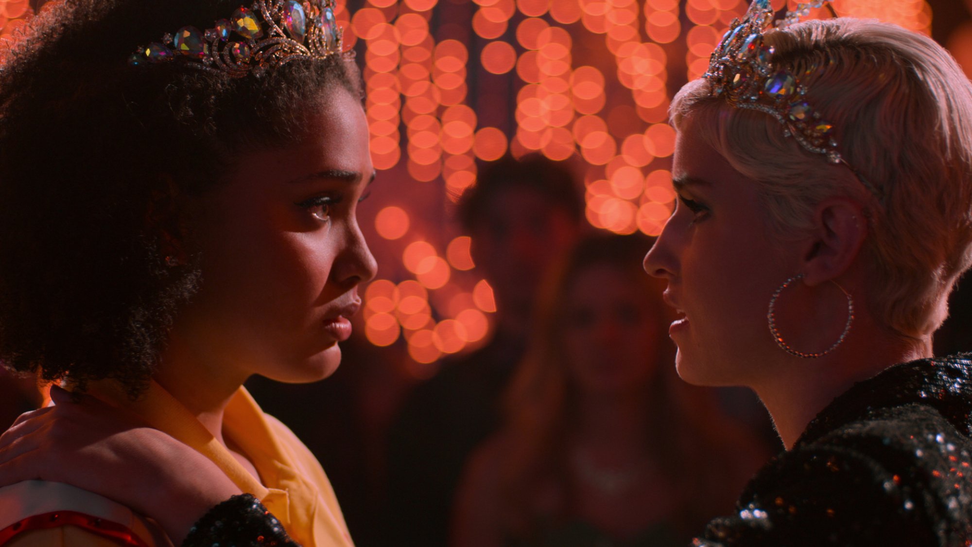 Two teen girls wearing crowns look into each other's eyes.