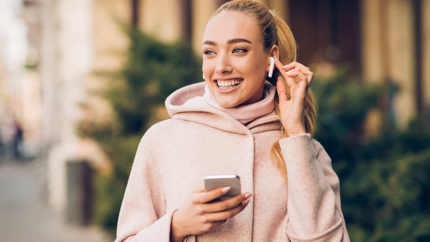 Smiling white woman holding iPhone with Airpods in ear