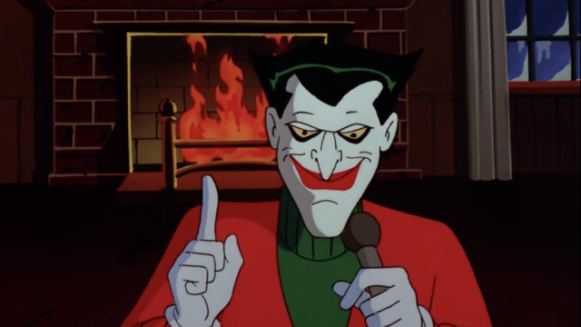 The Joker, dressed for Christmas, addresses the audience in front of a blazing hearth, in “Christmas with the Joker,” from Batman: The Animated Series.