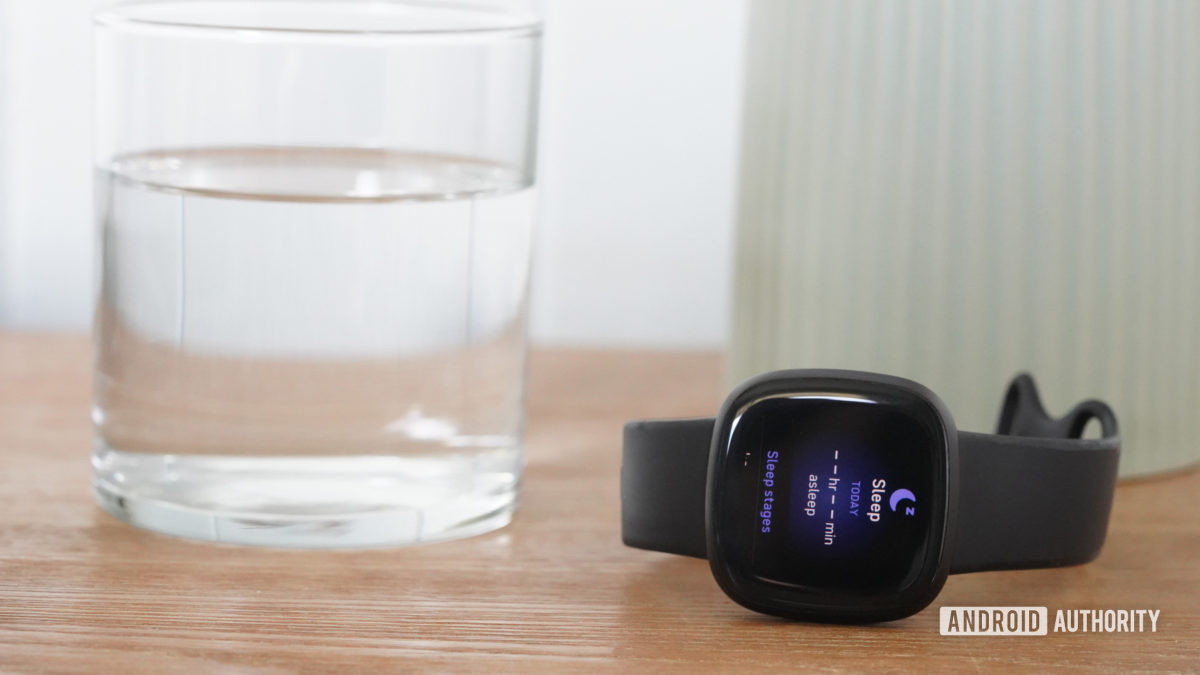 A Fitbit Versa 3 displays empty Sleep Data fields while resting on a bedside table.