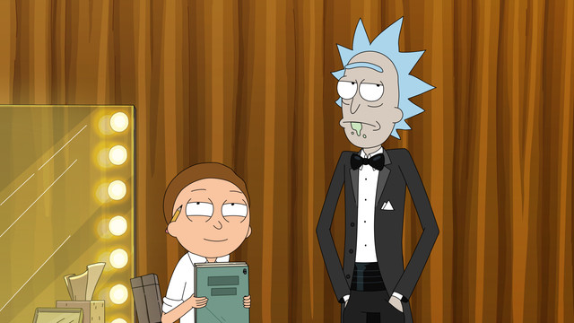 Rick and Morty standing backstage with a lighted mirror behind them; Rick is in a suit looking annoyed and Morty holding a clipboard looking pleased