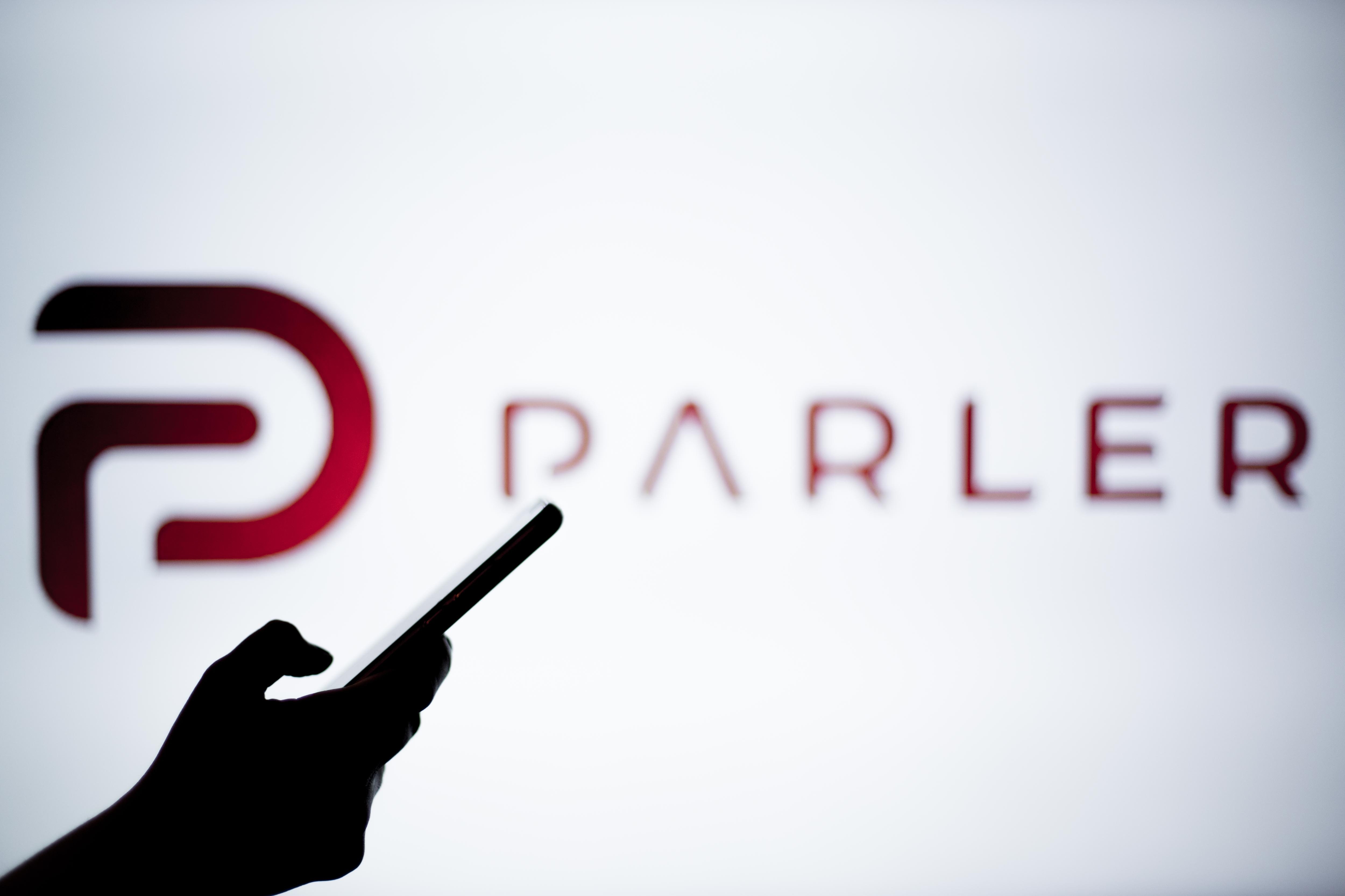A silhouetted hand holds a phone in front of the Parler logo.