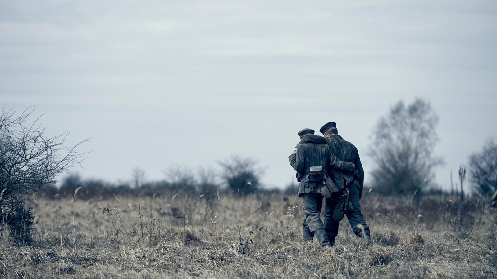 Two soldiers walk on a field arms wrapped around each other 