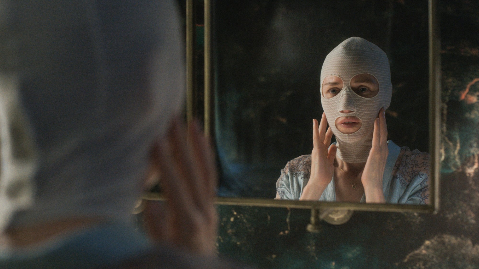 A woman in face bandages looks in a mirror