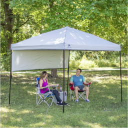 Two people sitting in camping chairs under the shade of an outdoor canopy