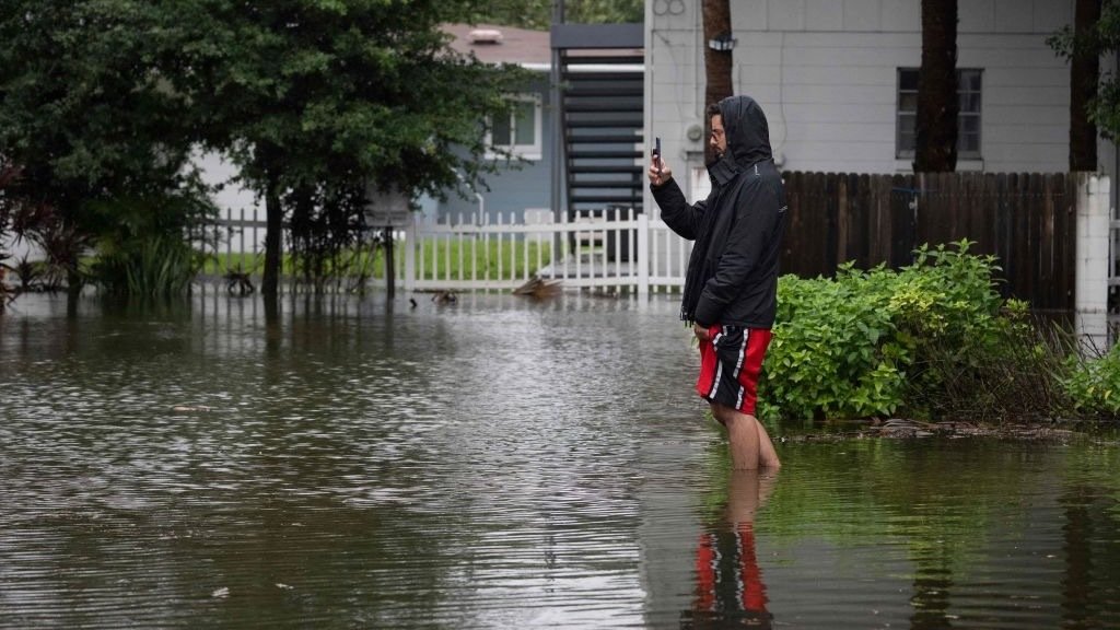 a man holding a phone in flood waters of hurricane ian