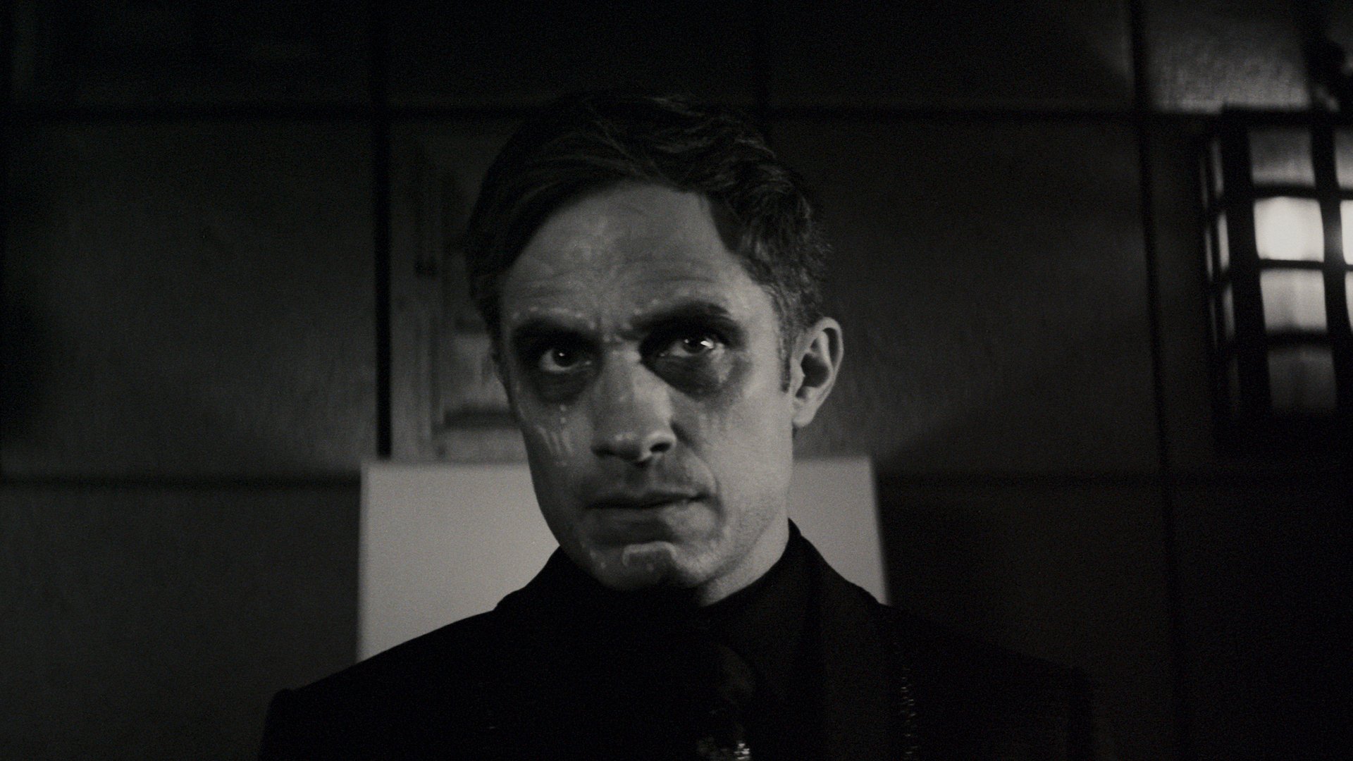 A black and white film still showing a man with face paint markings.