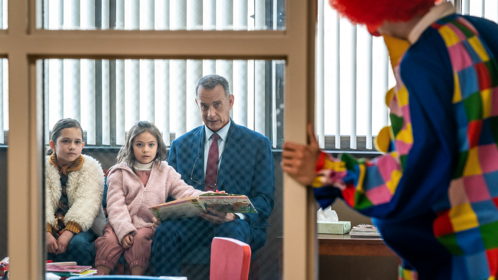 Tom Hanks reads a book to two young girls with a clown nearby, 