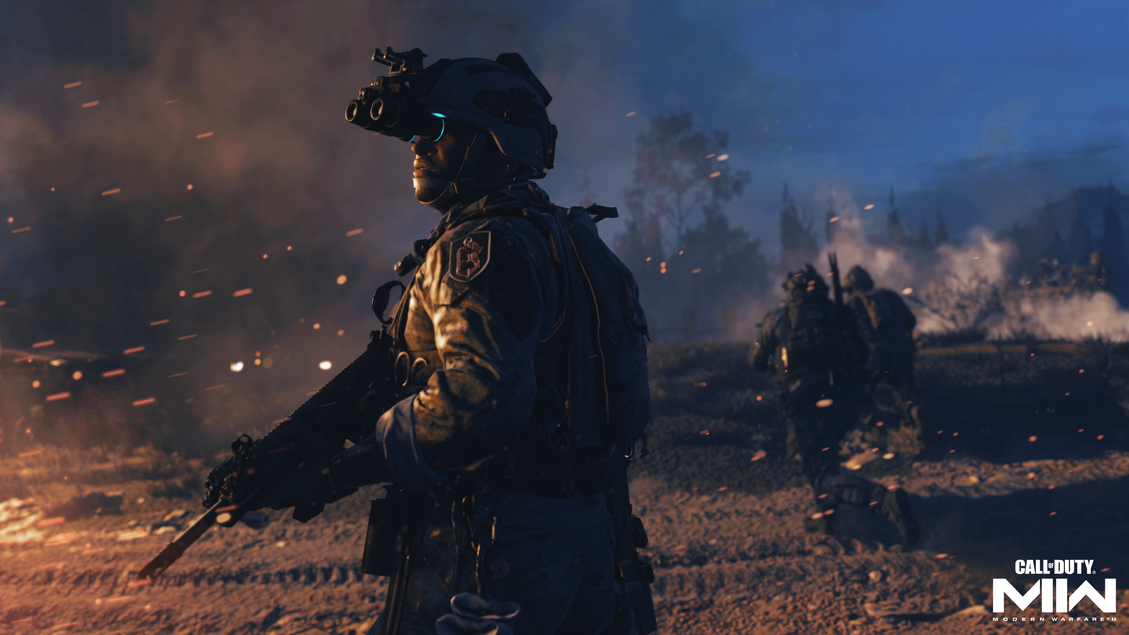 solider wearing nightvision googles looks out to the distance as the field around him is in flames