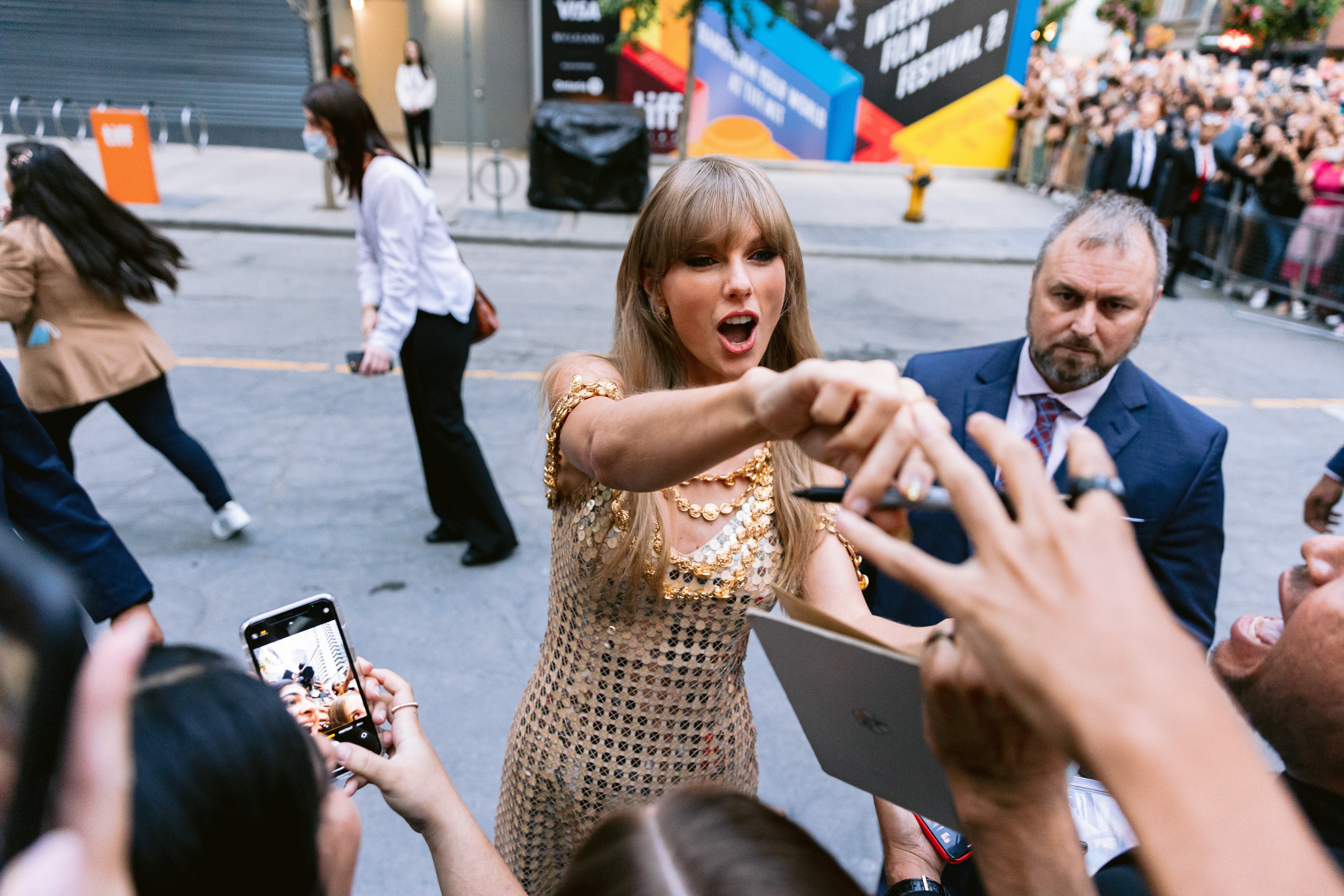 Taylor Swift in a gold dress interacting with fans. 