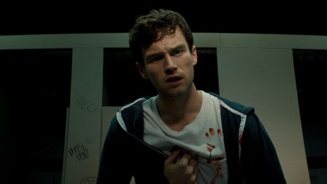 Brandon Flynn gives a puzzled expression with blood on his shirt and his fist to his chest in Hellraiser.
