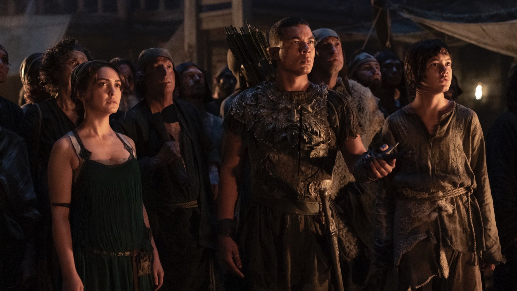 A human woman, her young son, and an elven man in armor stand at the front of a worried crowd.