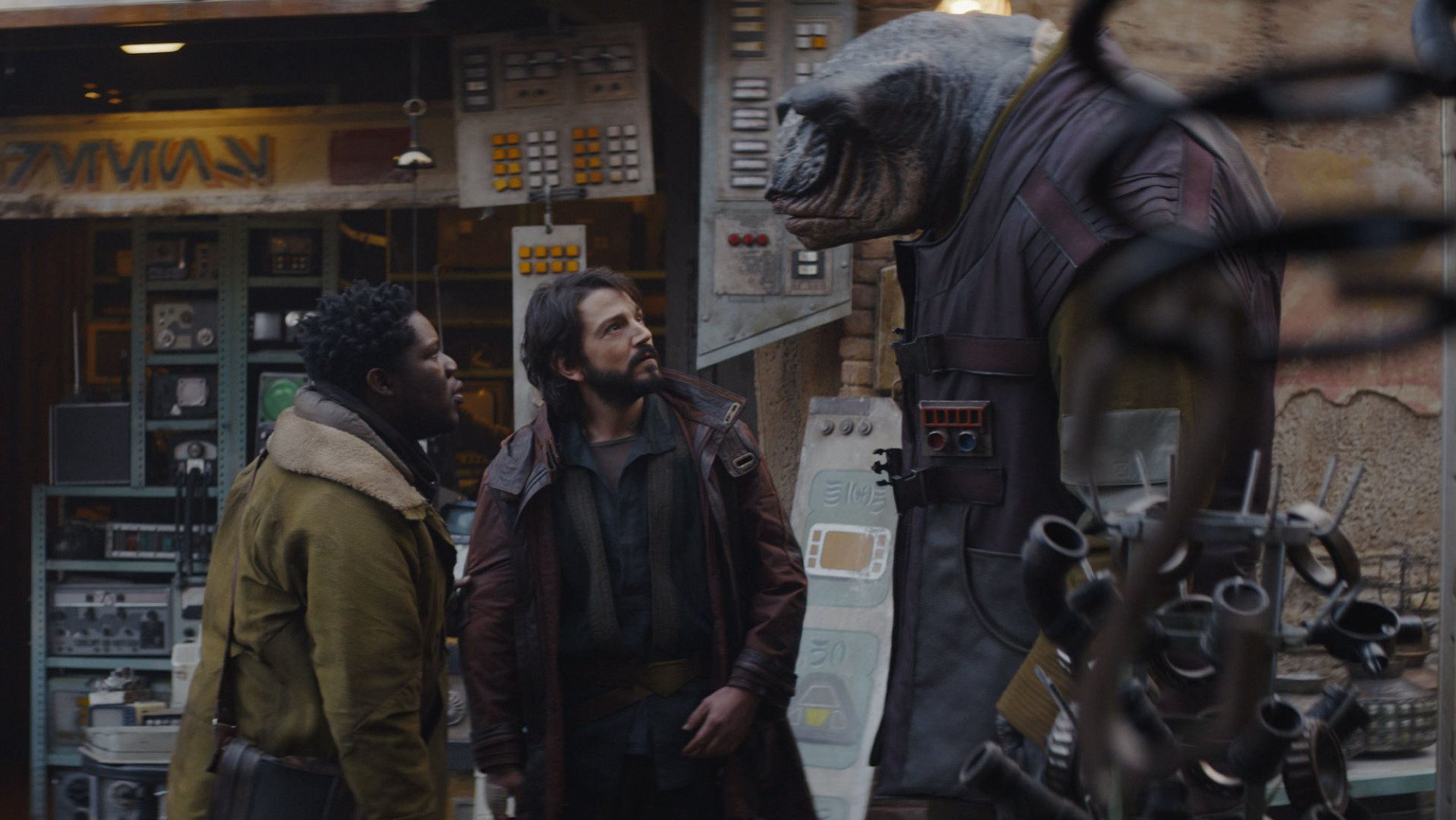 Two men and an alien stand on a sci-fi series set.