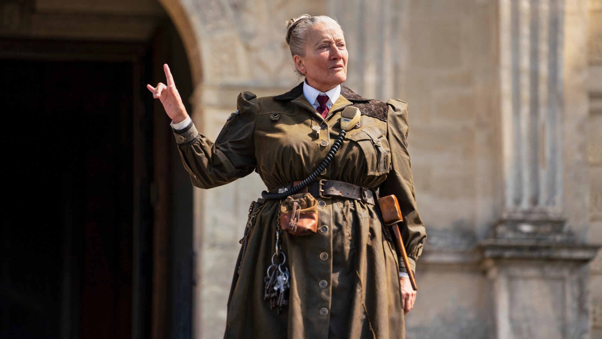 A headmistress wearing a military-style uniform raises a pointed finger.