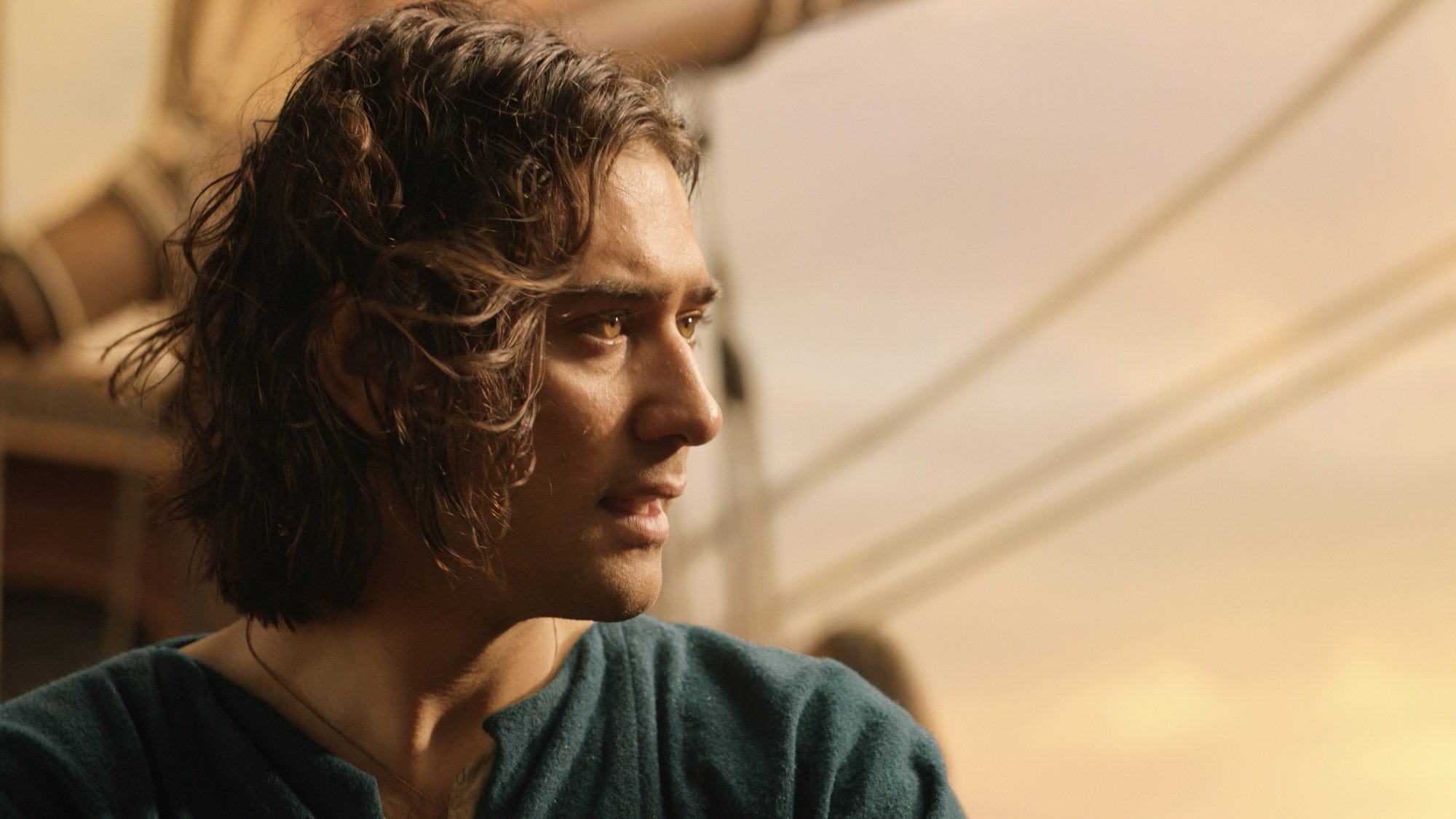 A man with medium-length brown hair stares at the sunset while on the deck of a ship.