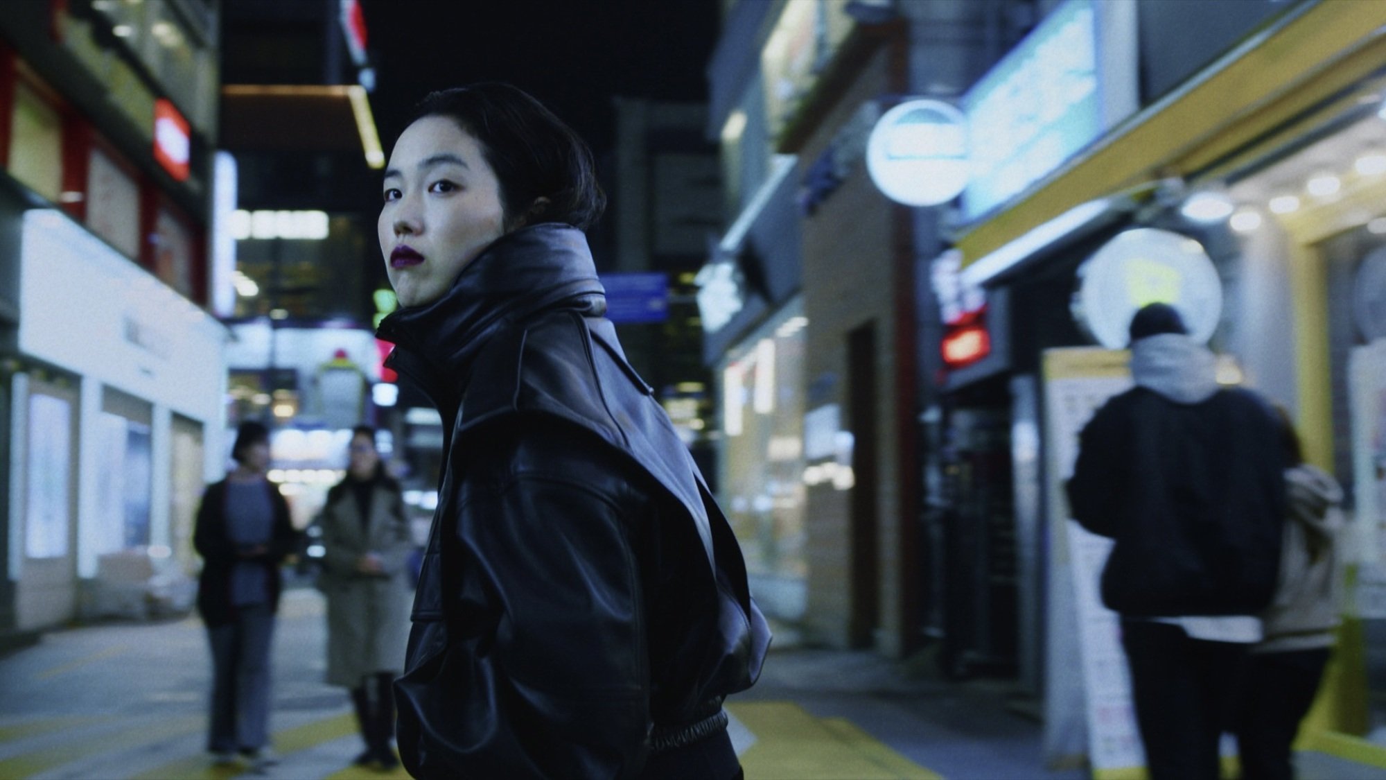 A woman in a high-collared black coat and lipstick on a Seoul street at night.