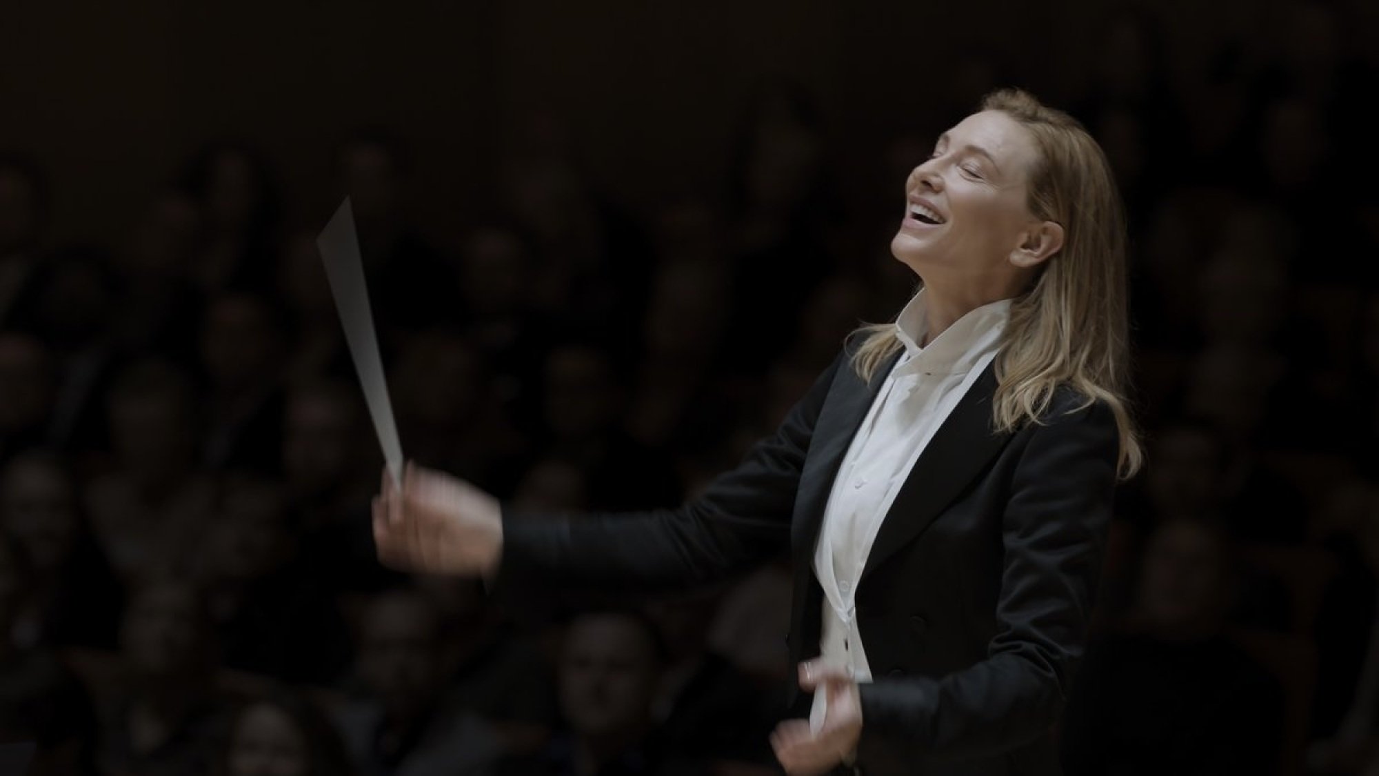 A woman in a suit conducts an orchestra.