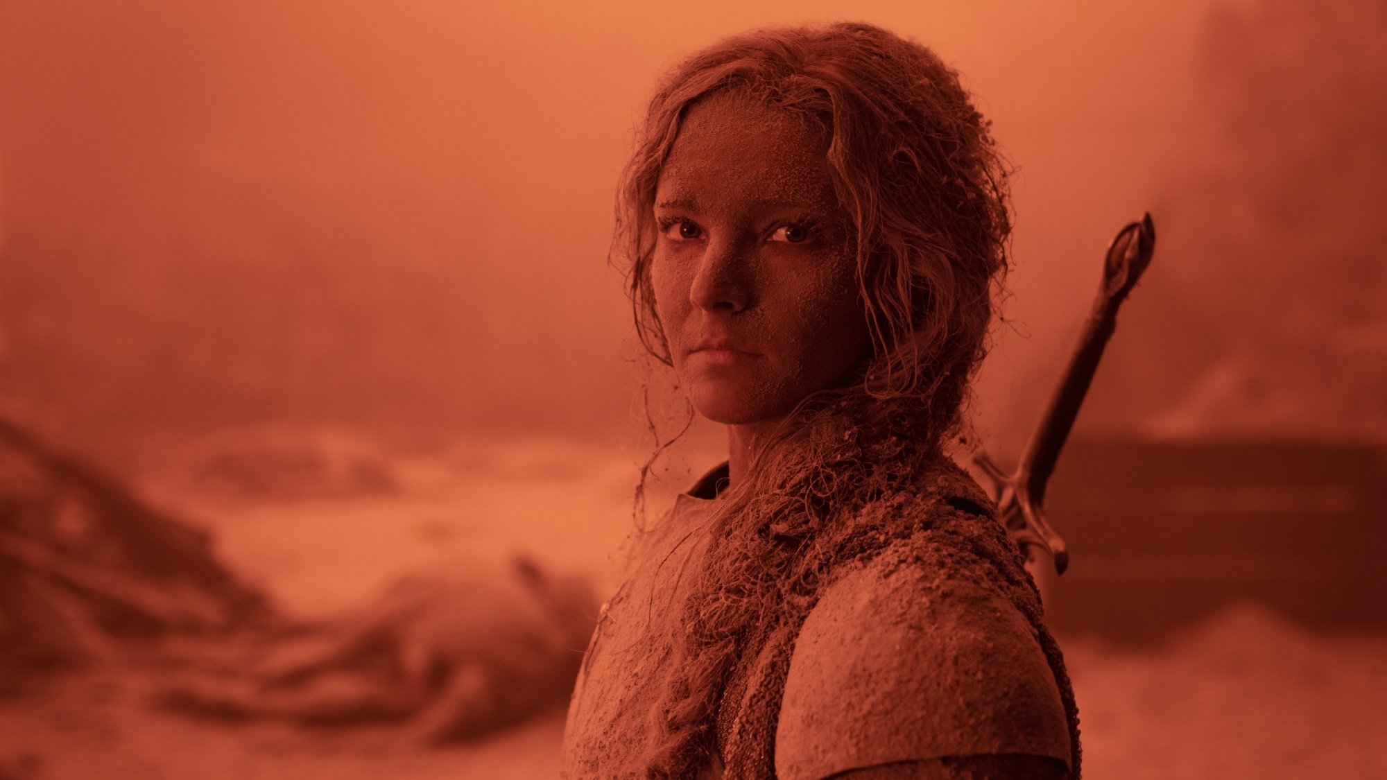 A blonde elf woman in armor stands in a red wasteland with ash coating her whole face and body.