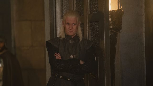 A mid-shot of Daemon standing and leaning against a wall with his arms folded in House of the Dragon