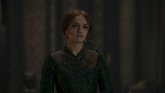 Queen Alicent stands in a green dress in her dimly lit room, hands folded in front of her as she looks toward the camera in something close to consternation, or maybe exhaustion, in HBO’s House of the Dragon.