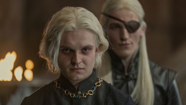 Aegon in the foreground looking grumpy about something, while his eyepatch-clad brother stands behind him out of focus, in House of the Dragon