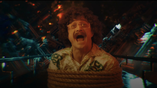 “Weird Al” Yankovic (Daniel Radcliffe), bound and stuck on a conveyer belt during an acid trip, stares into the camera and screams in Weird: The Al Yankovic Story