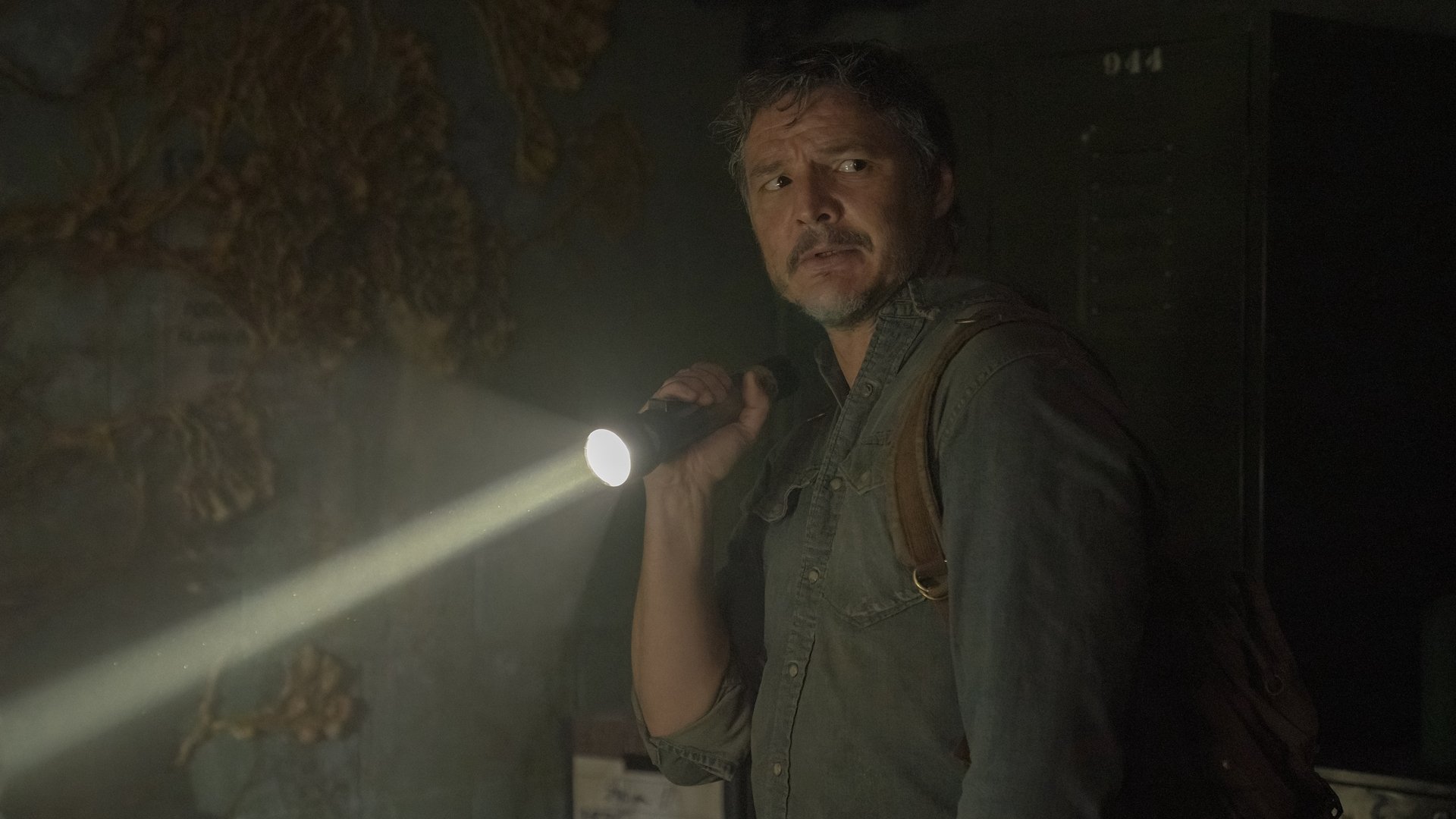 A man stands in a dark abandoned room with a flashlight.